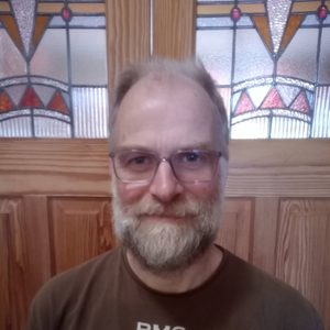 David is looking at the camera. He is standing in front of a stained glass window.