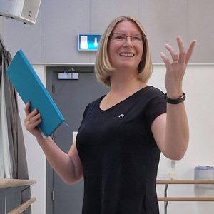 Eilidh is gesturing off-camera. She is holding a document.