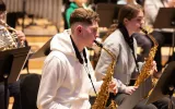 Photograph of saxophone players playing as part of an orchestra.