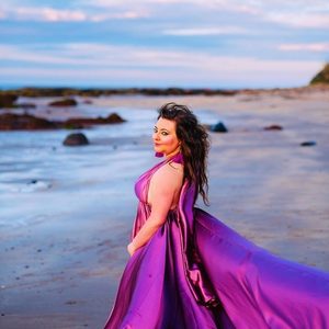 Alison is standing at the beach. She is wearing a brightly coloured dress.