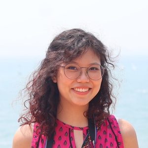 Pimlabhas is smiling at the camera. She is wearing a pink top and glasses.