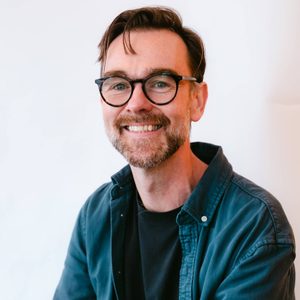 Alan is smiling at the camera. He is wearing a blue shirt.