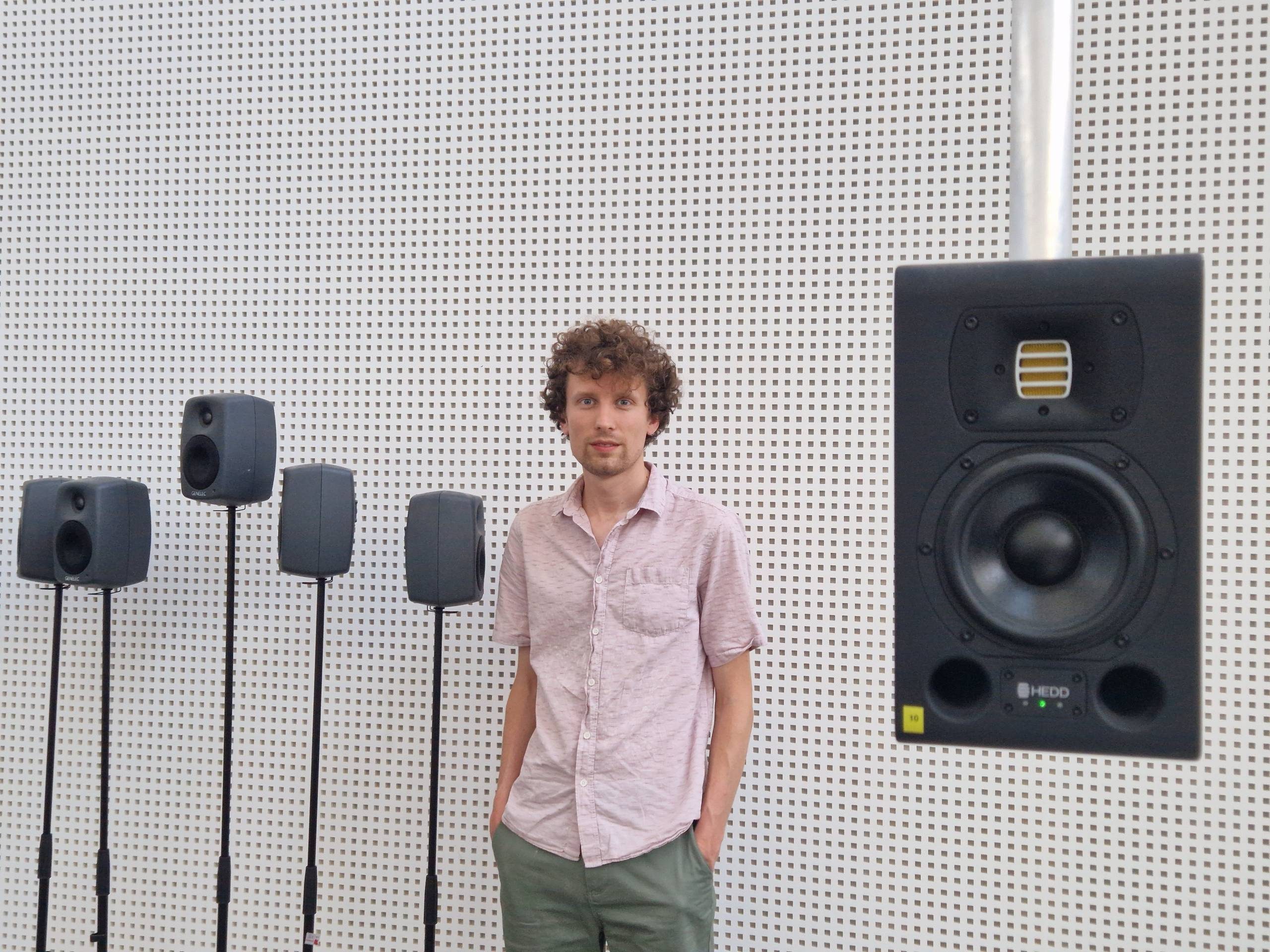 Robert is standing next to speakers. He is looking at the camera.