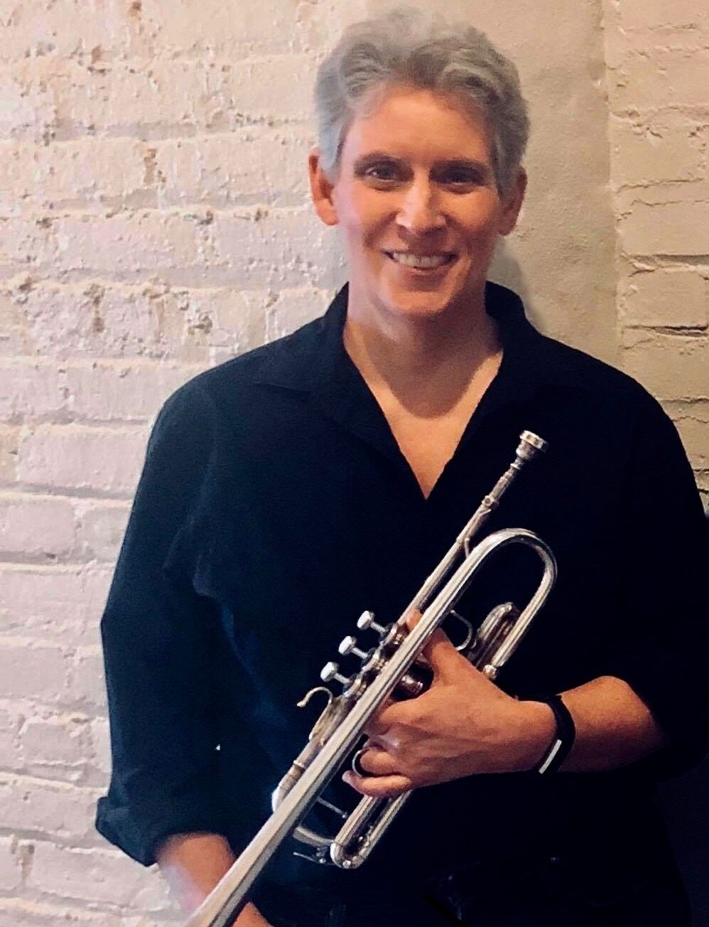 Sandy is smiling at the camera. She is holding a trumpet.