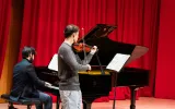 A violin player in front of a piano